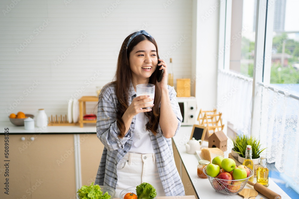 Young Asian women wake up in the morning and drink fresh milk for breakfast in the kitchen with different type of salad vegetable and healthy food. Good nutrition eating human body condition.
