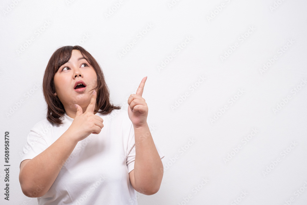 Young beautiful Asian oversize chubby women smile with positive emotion and point finger to copy space area, feeling happy and proud with her body size. Portrait shot on white background. Young beautiful Asian oversize chubby women smile with positive emotion and point finger to copy space area, feeling happy and proud with her body size. Portrait shot on white background.