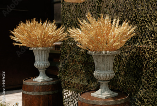 Dried flowers of wheat stand in a gray vase on a military background