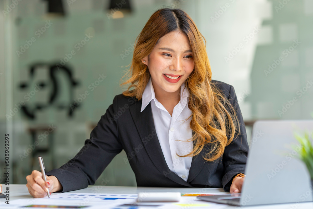 Asian businesswoman working on laptop and taking notes at the office