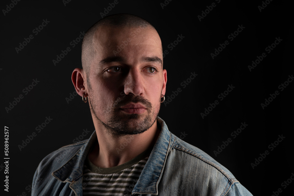 handsome man with calm bristled view in jeans jacket isolated in studio on black background