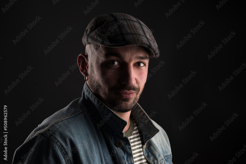 Stylish young man in beret calmly looking at camera. Portrait of trendy man in cap and denime with slight smile and calmness expressing kindness in his eyes