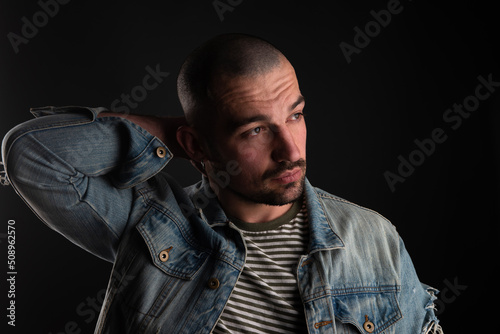 Portrait of calm glance of handsome bristled man in denime jacket looking away with his arm behind his head photo