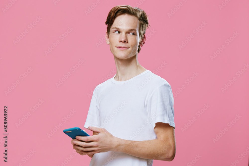 portrait of a young man on a pink background in a white shirt stands smiling with a phone in his hands. Studio photography with space for text portrait of a young man on a pink background in a white shirt stands smiling with a phone in his hands. Studio photography with space for text