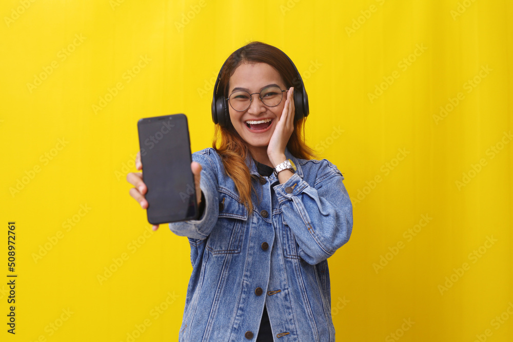 Happy expression of young asian woman showing a blank cellular phone screen while using a headphone Happy expression of young asian woman showing a blank cellular phone screen while using a headphone