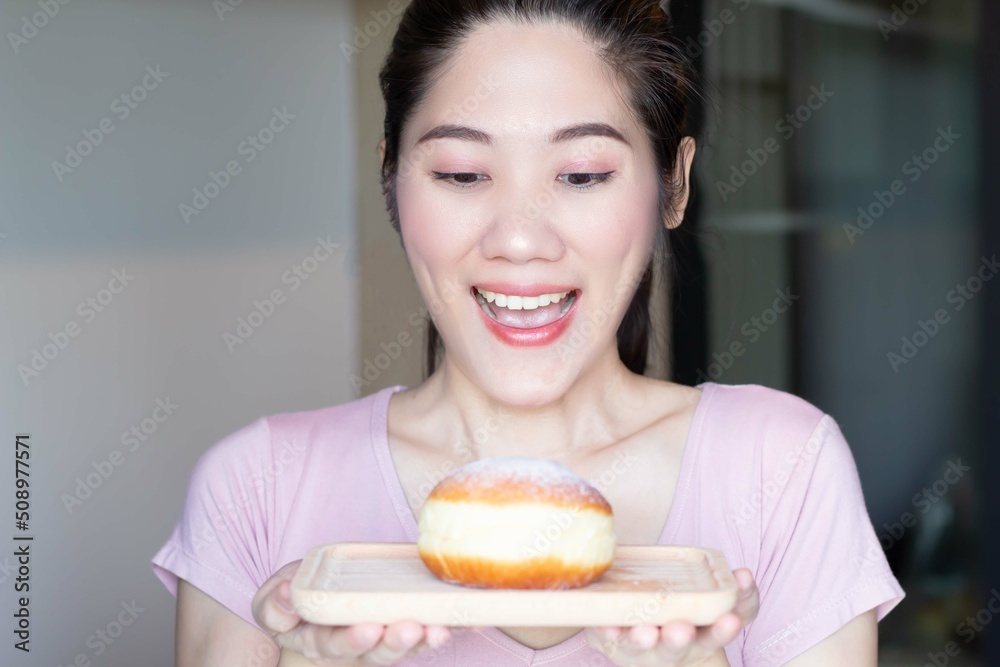 Asian beautiful woman are holding and looking to doughnut bun on wooden plate and open mouth and smile with excited to eat it. Asian beautiful woman are holding and looking to doughnut bun on wooden plate and open mouth and smile with excited to eat it.