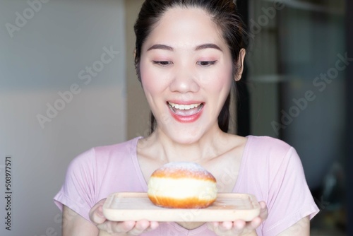 Asian beautiful woman are holding and looking to doughnut bun on wooden plate and open mouth and smile with excited to  eat it.