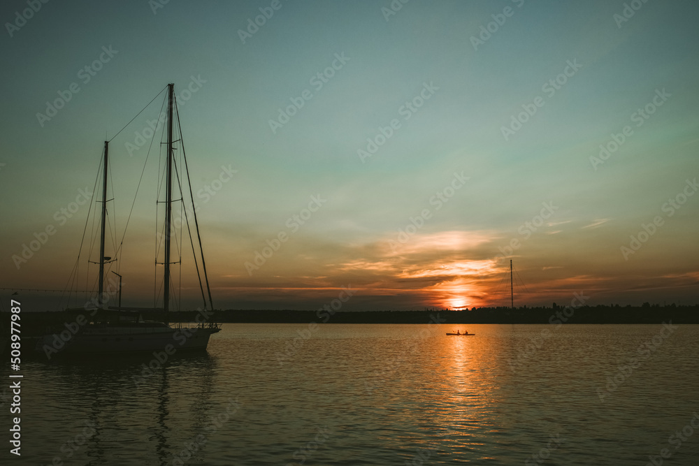 Sunset in the river coast side, sun reflects into the water surface. Yachts and boats near the beach