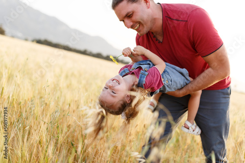 Happy father playing and carrying his daughter on hands.Mature man playing with his little daughter in nature.Smiling happy father playing with daughter in park and hugging her