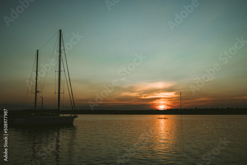 Sunset in the river coast side, sun reflects into the water surface. Yachts and boats near the beach © Евгения Жигалкина