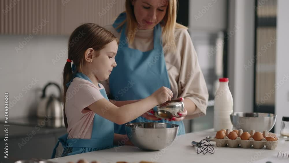 little girl is helping to her mom in kitchen, mother and daughter are cooking together, adding sugar little girl is helping to her mom in kitchen, mother and daughter are cooking together, adding sugar