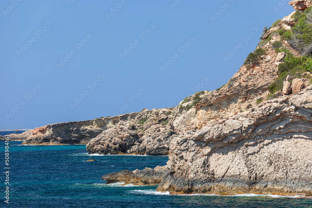 Morning view of the sea and sun-bleached coastal cliffs of Ibiza island under clear, pale blue sky without a single cloud, Balearic Islands, Spain