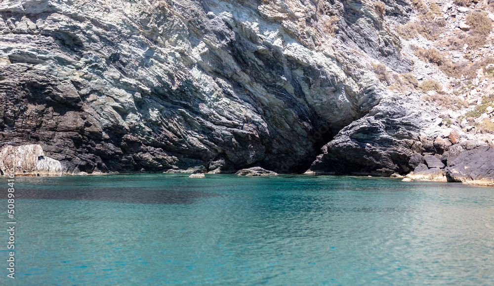 Aegean Sea. Rocky coast, cliff and cave, Cyclades Greece, Rippled water near Nios island