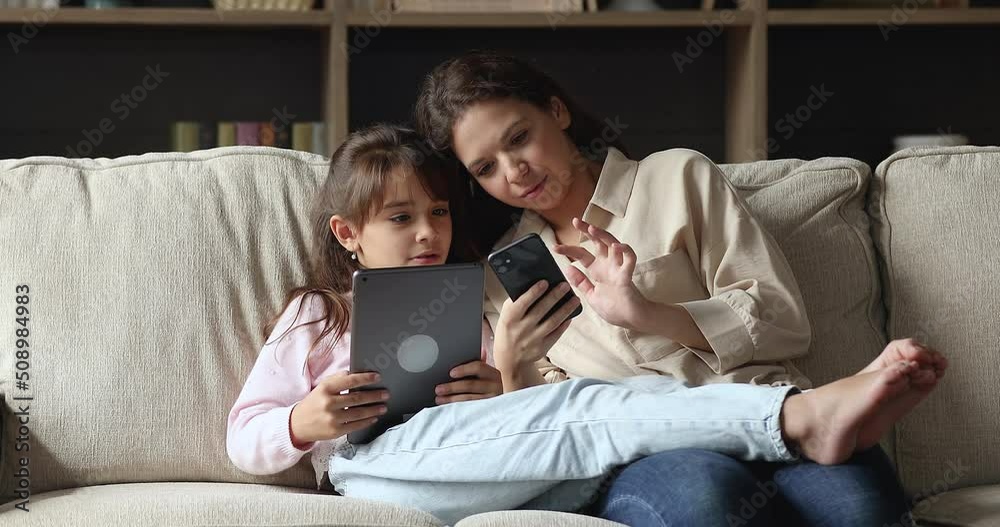 Young mom holds smartphone her daughter use digital tablet spend leisure at home with wireless gadgets, have fun, discuss new cool app. Young gen and modern tech overuse, on-line games users concept Young mom holds smartphone her daughter use digital tablet spend leisure at home with wireless gadgets, have fun, discuss new cool app. Young gen and modern tech overuse, on-line games users concept