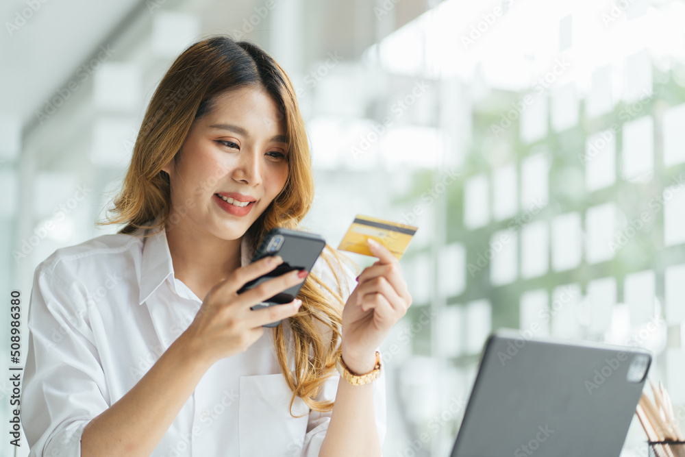 Young woman holding credit card and using smartphone, Girl working online. Online shopping, e-commerce, internet banking, spending money, working from home concept. Young woman holding credit card and using smartphone, Girl working online. Online shopping, e-commerce, internet banking, spending money, working from home concept.