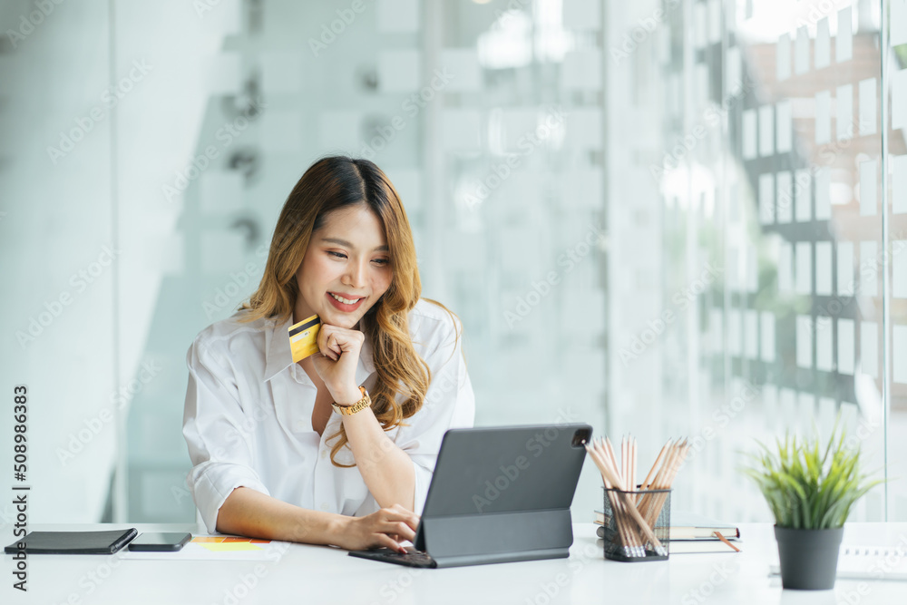 Young woman holding credit card and using laptop computer. Girl working online. Online shopping, e-commerce, internet banking, spending money, working from home concept Young woman holding credit card and using laptop computer. Girl working online. Online shopping, e-commerce, internet banking, spending money, working from home concept