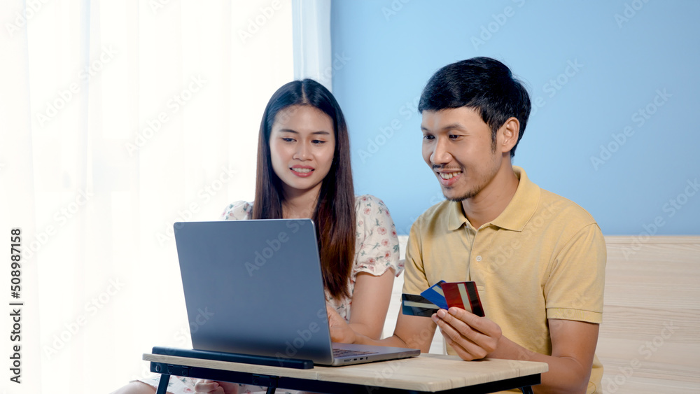 Young Asian man, couple looking at shopping, and ordering online via laptop computer, two people choosing a credit card to pay for their purchases.,online shopping. Young Asian man, couple looking at shopping, and ordering online via laptop computer, two people choosing a credit card to pay for their purchases.,online shopping.