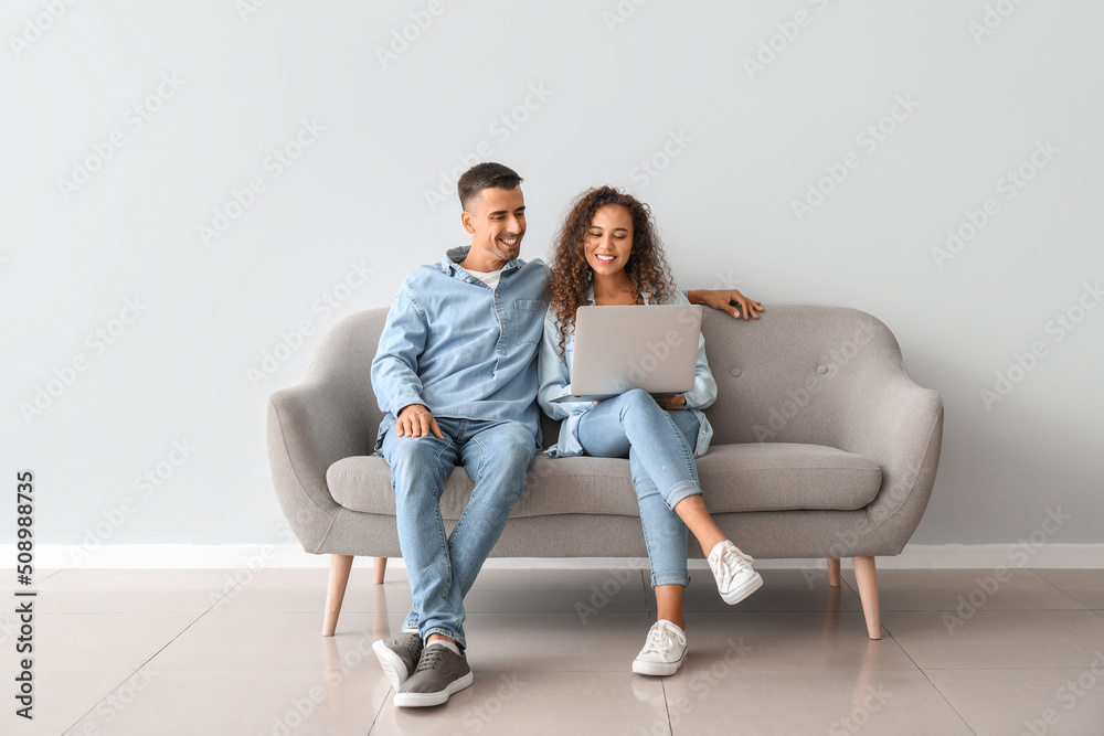 Young couple with laptop sitting on sofa near light wall Stock Photo ...