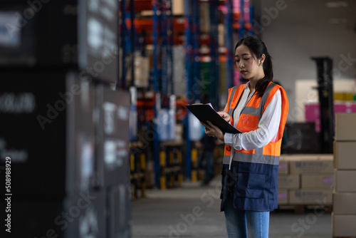 Professional beautiful asian woman worker checks stock and inventory with holding clipboard in the retail warehouse full of shelves with goods. Working in logistics, Distribution center.