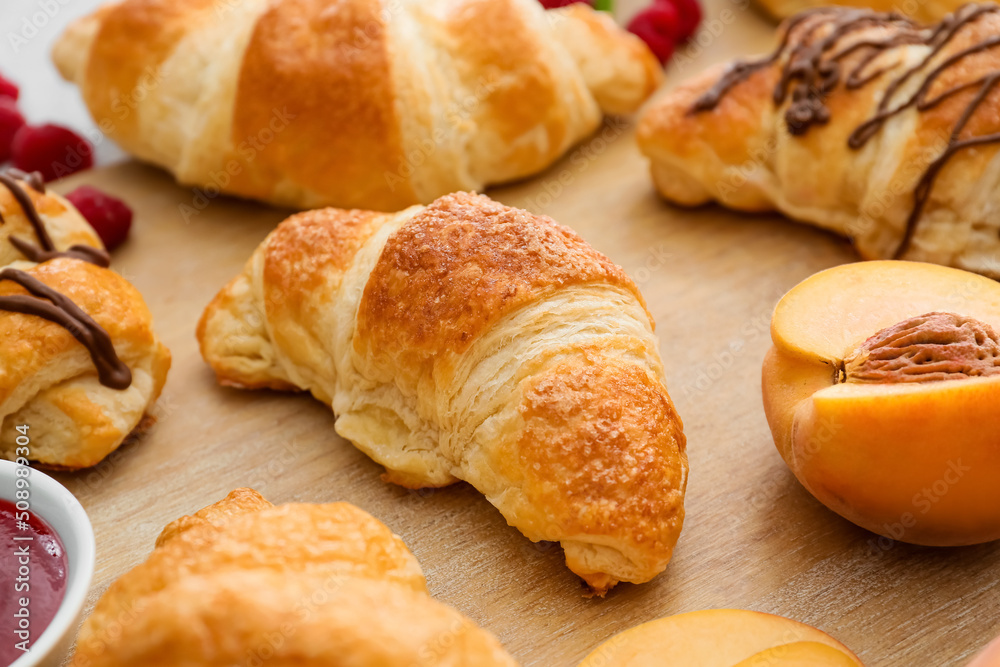 Wooden board of delicious croissants with peach on table, closeup