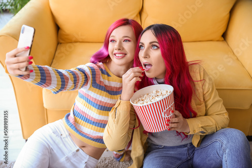 Beautiful women with popcorn taking selfie at home