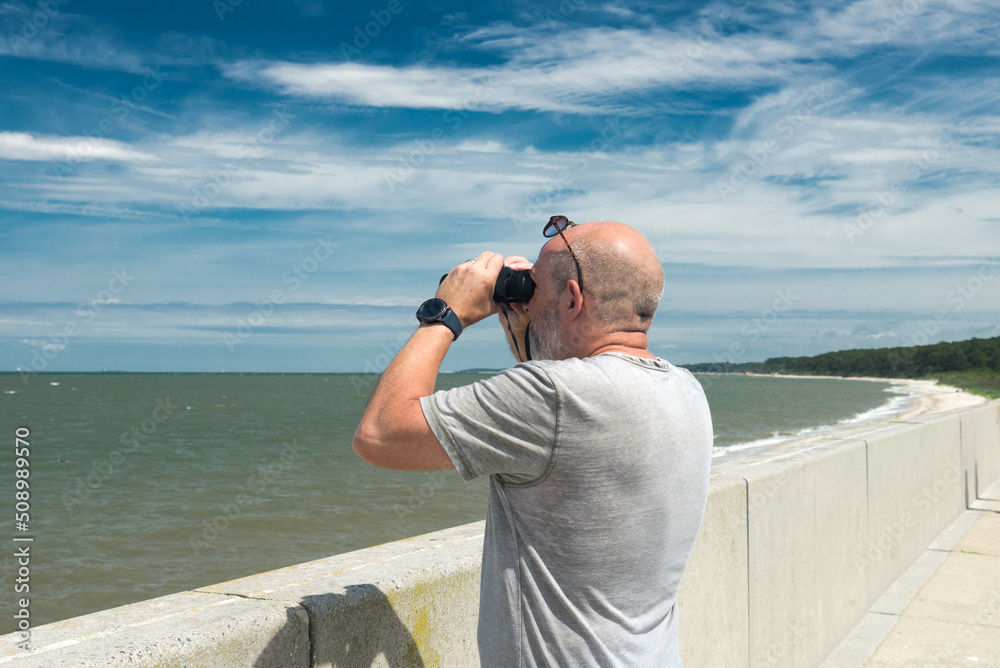 Obraz premium man watches the ocean through binoculars on a summer sunny day.