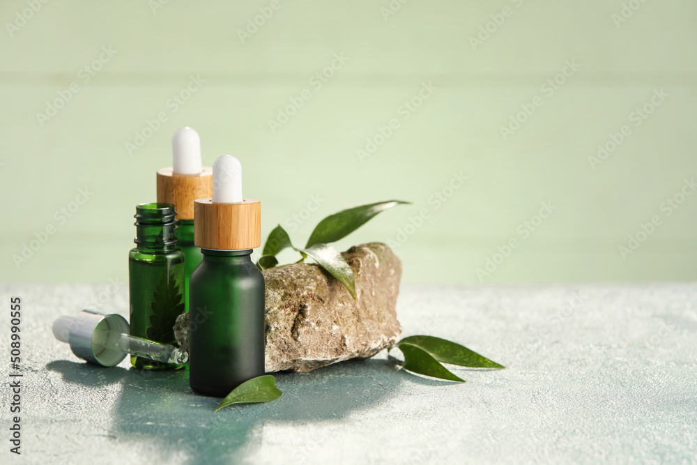 Bottles of natural serum, stone and plant leaves on green table Bottles of natural serum, stone and plant leaves on green table