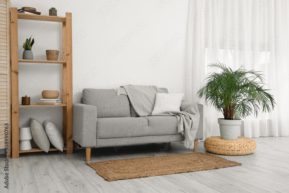 Interior of light living room with grey sofa, shelving unit and