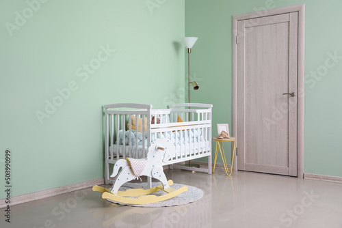 Interior of stylish nursery with baby crib, lamp and rocking horse photo