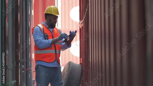African American cargo container man hold tablet and walk along the channel between the tank to inspect and check safety of product in workplace area.