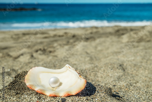 Beautiful pearl in the pearl shell on the sand beach. Sea and blue sky.