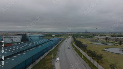 Forwards fly above road loading in industrial suburb on cloudy day. Large cylindrical tanks for materials in factory. Port Elisabeth, South Africa