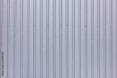 Gray profiled fence made of galvanized corrugated board with vertical rails.