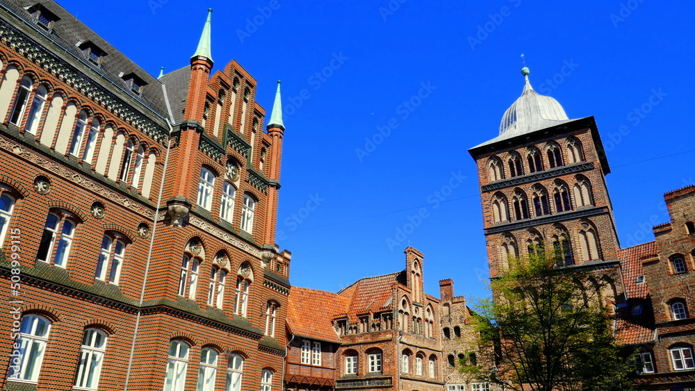 prunkvolle alte Backsteinhäuser in der Altstadt von Lübeck und hohem Burgtorturm unter blauem Himmel