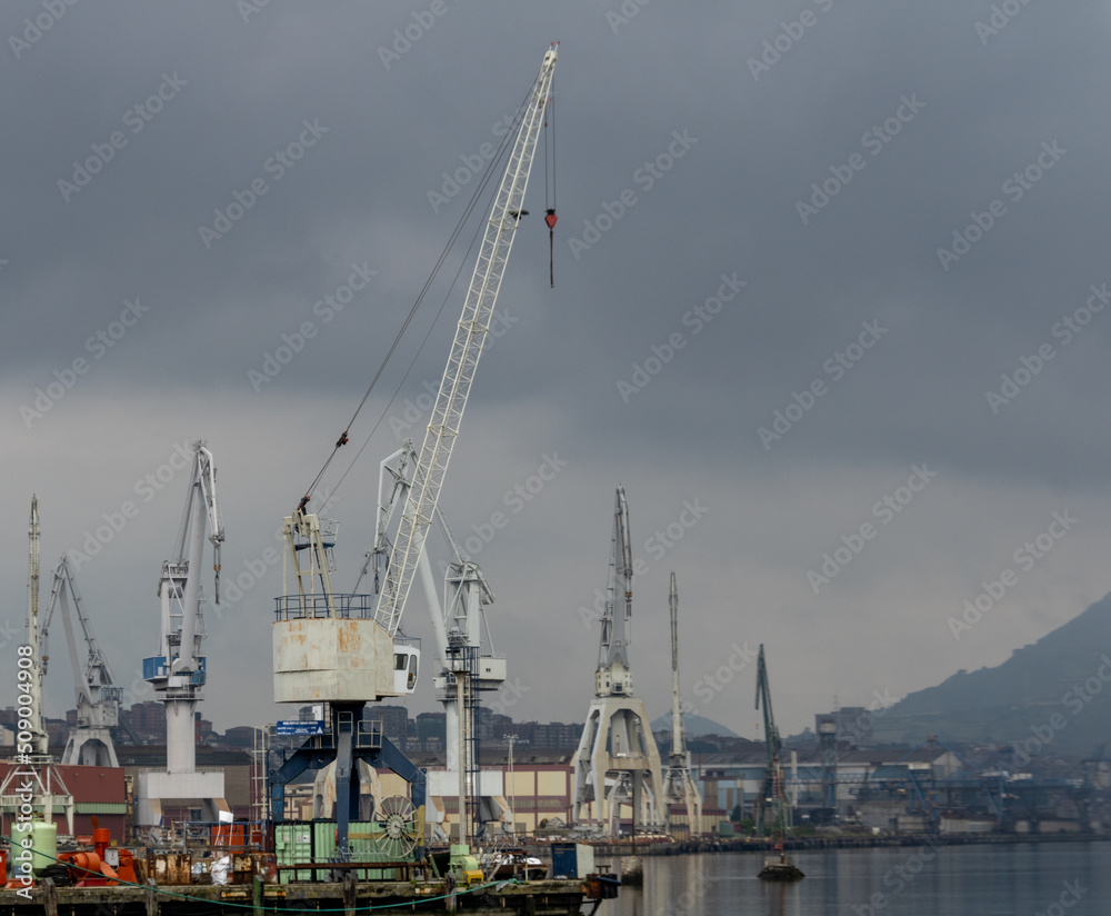 cranes and ships near the Basque estuary ready for industry with the estuary calm under cloudy skies on a spring day