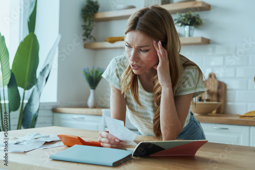 Stressed young woman calculating finances while standing at the domestic kitchen photo