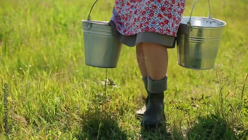 Close-up of a milkmaid carrying buckets and walking through tall grass photo