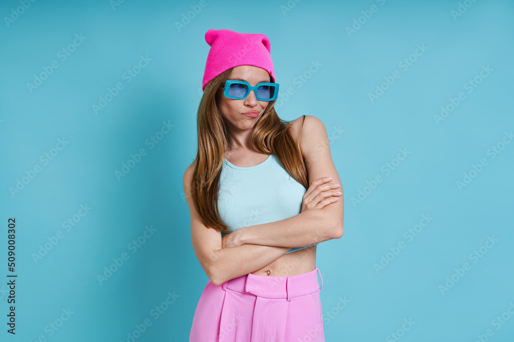 Young woman in pink hat looking displeased while standing against blue background Young woman in pink hat looking displeased while standing against blue background