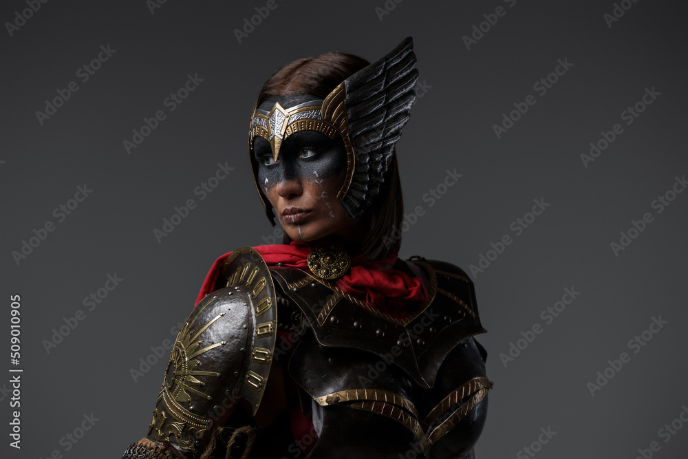 Shot of female warrior with painted face dressed in dark armor and red cape.