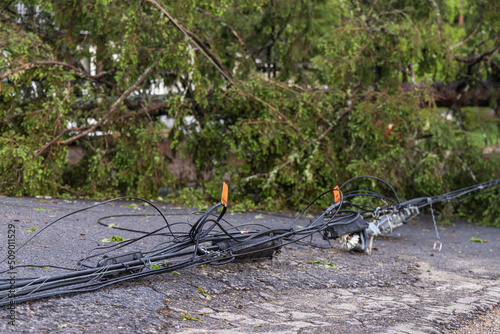 Closeup selective focus view of dangerous electricity supply wires lying across tarmac of main road after high winds bring down overhead power lines.