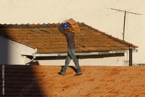 Roofer working on roofing construction. Bricklayer roof repair. House under construction. Workman renovates waterproofing roof of building. Carpenter construction worker carry pile of tiles