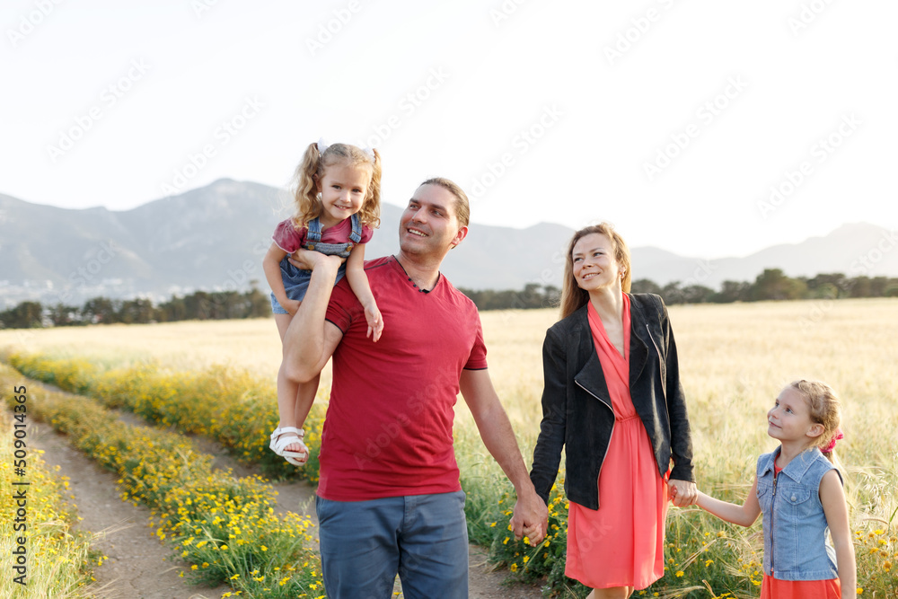 Happy family father of mother and two daughters sisters walking on countryside nature at sunset.Carefree parents having fun with their kids on a field. Happy family father of mother and two daughters sisters walking on countryside nature at sunset.Carefree parents having fun with their kids on a field.