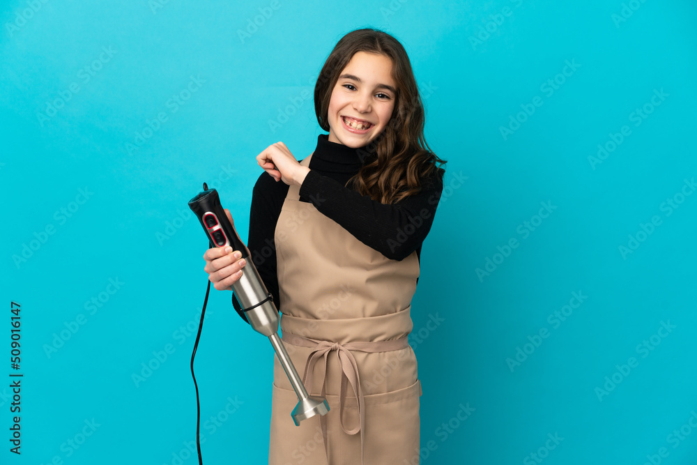 Little girl using hand blender isolated on blue background celebrating a victory Little girl using hand blender isolated on blue background celebrating a victory