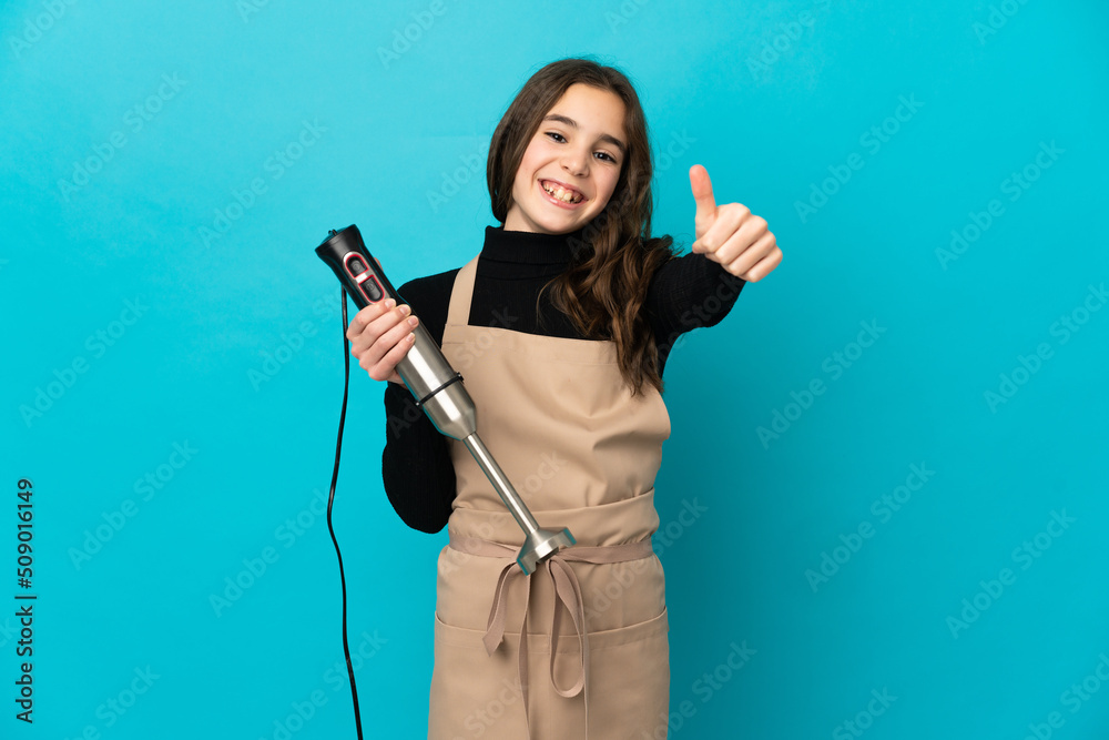 Little girl using hand blender isolated on blue background with thumbs up because something good has happened Little girl using hand blender isolated on blue background with thumbs up because something good has happened