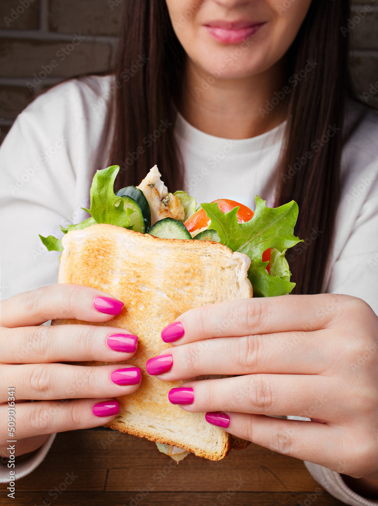 Young woman is holding a delicious sandwich in a cafe. Lunch, dinner, snack, branch. Young smiling woman was going to eat. Fast food concept. Copy space. Close up. Serving dishes in the restaurant.