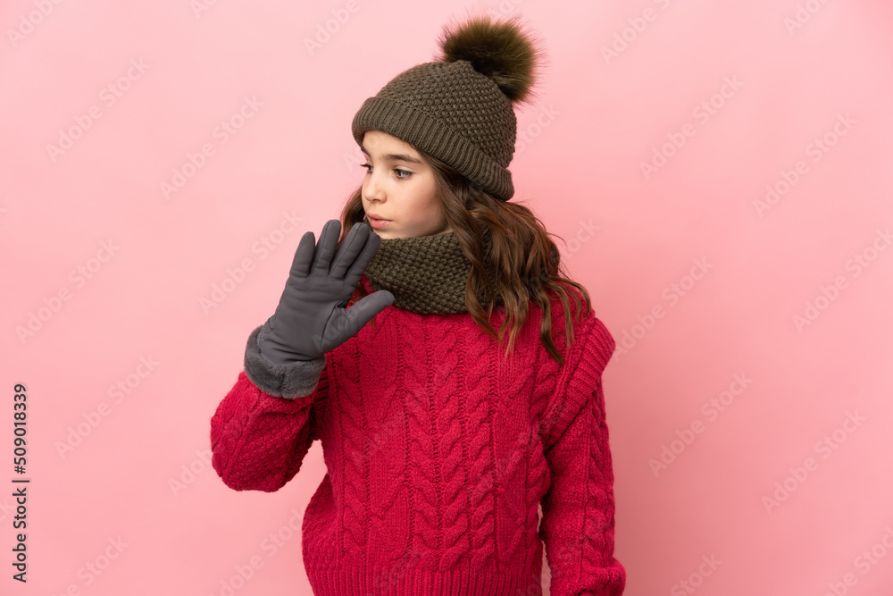 Little girl with winter hat isolated on pink background making stop gesture and disappointed