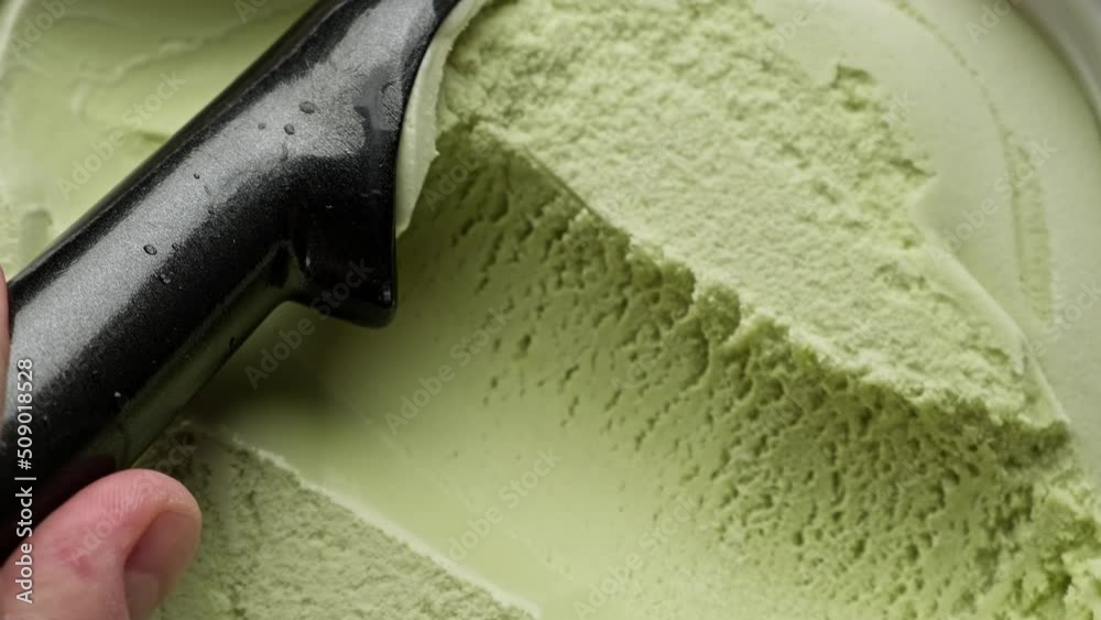Flavored pistachio ice cream scooping out of container by spoon. Top view of surface of green ice cream. Delicious dessert. Close-up in 4K, UHD