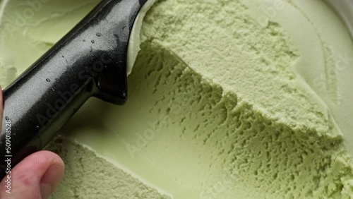 Flavored pistachio ice cream scooping out of container by spoon. Top view of surface of green ice cream. Delicious dessert. Close-up in 4K, UHD photo