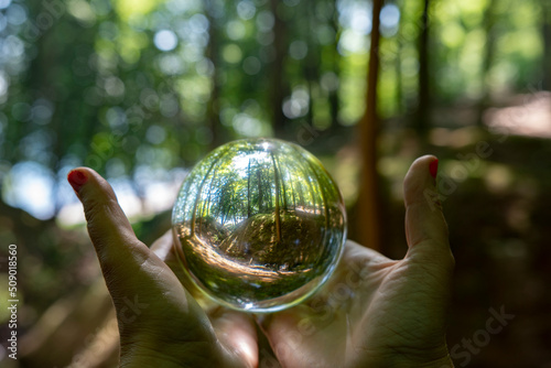 Womans hands with red nail polish holdin a crystal ball with nature inside and in nature