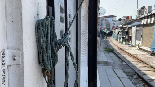 Rope cord hanging on wall pulls outdoor umbrella at local Maeklong market (Talad Rom Hub), popular tourist destination. Train track on ground - day   